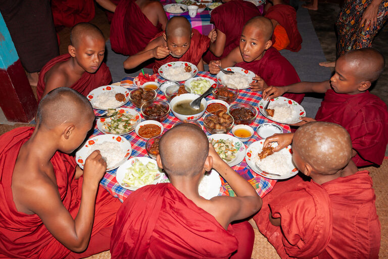 reich gedeckter runder Tisch mit 7 essenden Mönchen